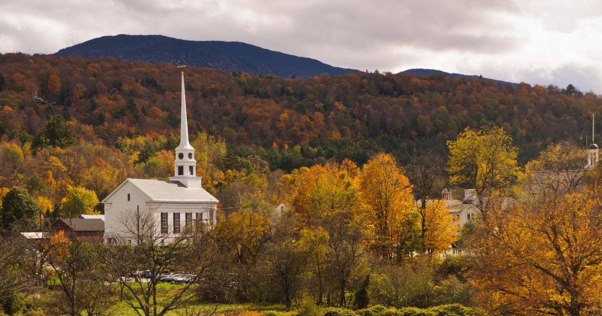 Vermont events and festivals featuring a quaint Vermont village with a church steeple among vibrant fall foliage.